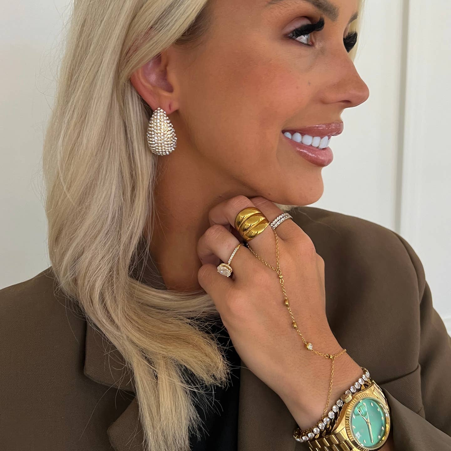 Woman wearing gold jewelry including earrings, rings, and a watch.