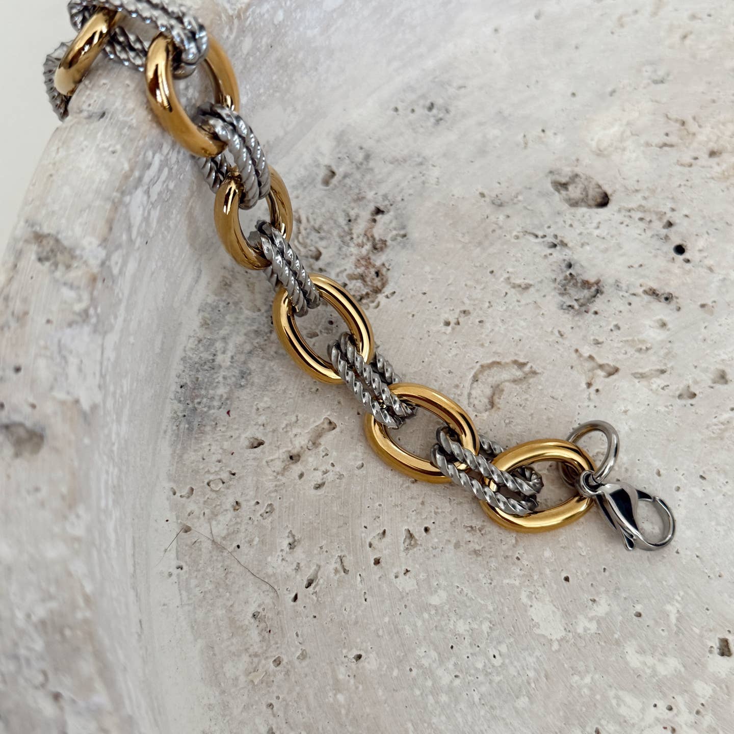 Gold and silver chain bracelet on a textured stone surface
