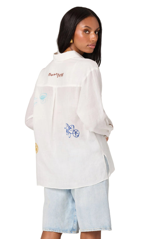 Woman wearing a white embroidered shirt with a plain background