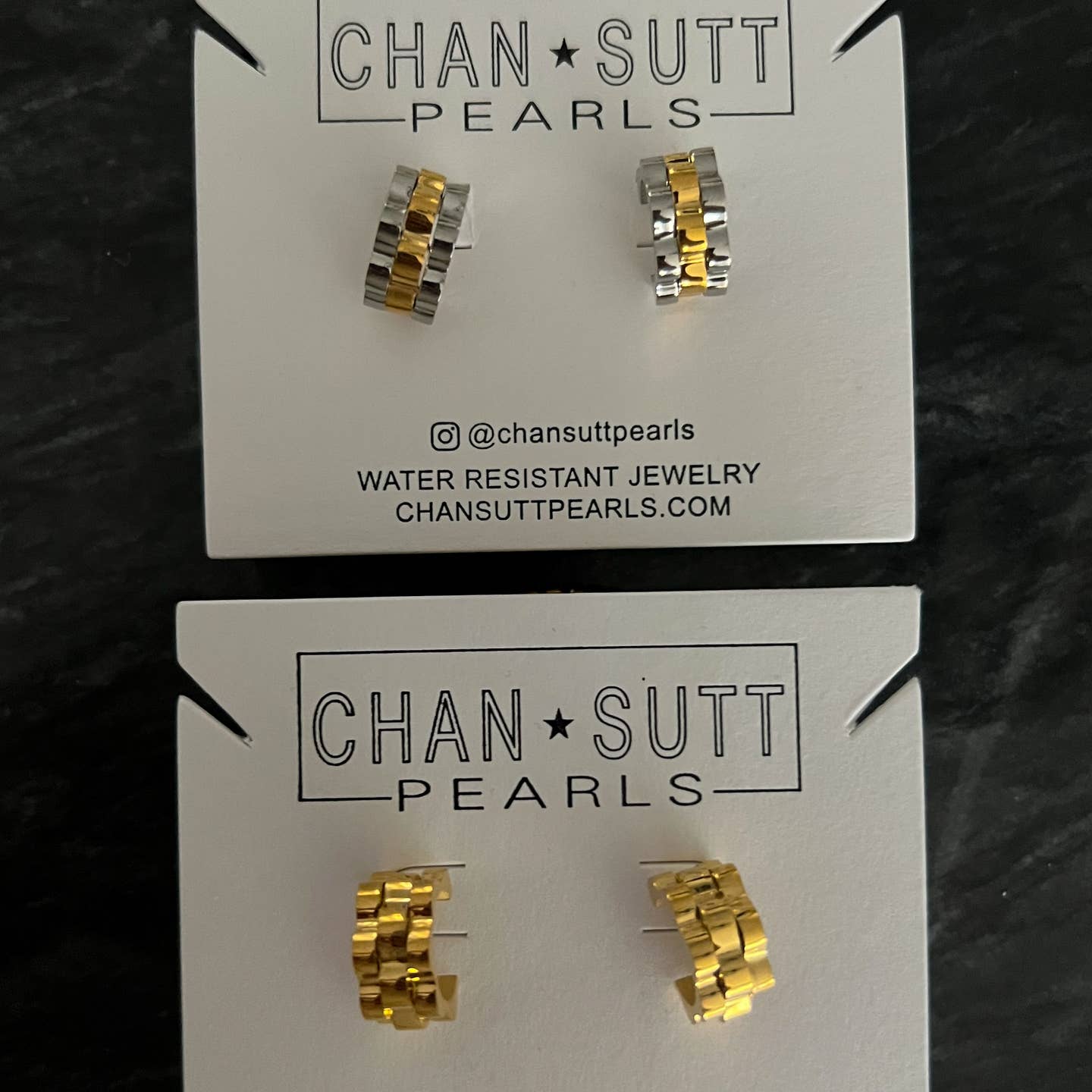 Gold and silver earrings on 'Chan Sutt Pearls' cards against a dark background