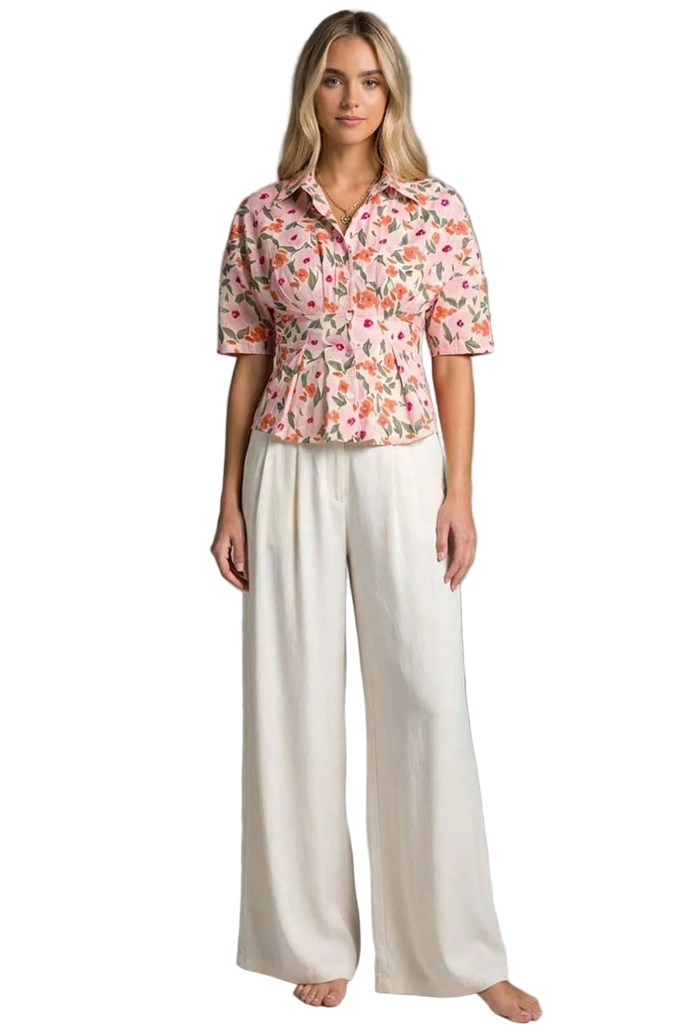Woman wearing a floral blouse and white pants against a gray background