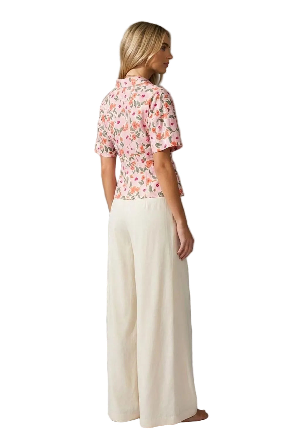 Woman wearing a floral blouse and white pants against a gray background