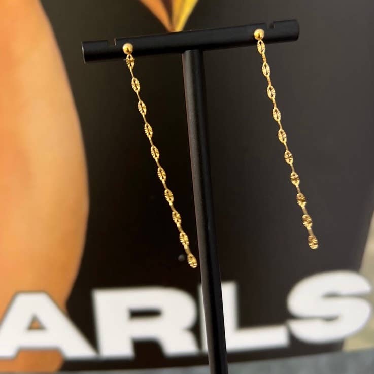 Gold chain earrings on a black stand with a blurred background