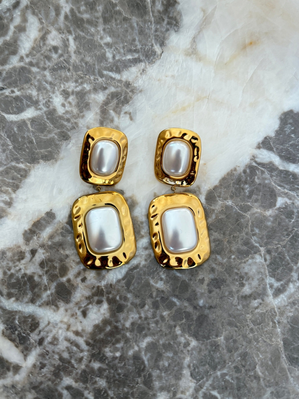 Gold earrings with pearl-like stones on a marble surface
