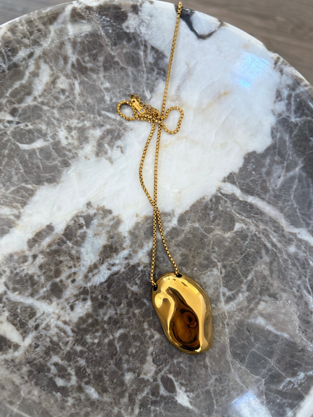 Gold necklace with a pendant on a marble surface