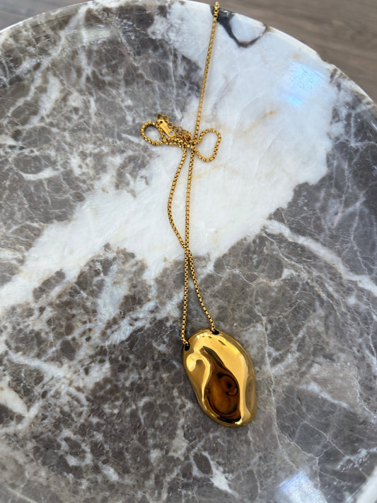 Gold necklace with a pendant on a marble surface