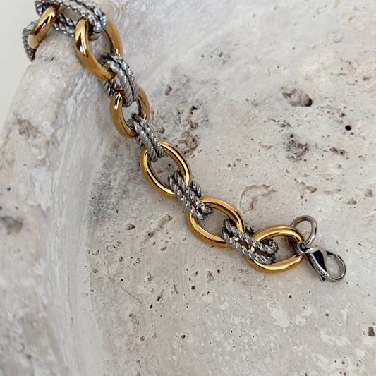 Gold and silver chain bracelet on a textured stone surface