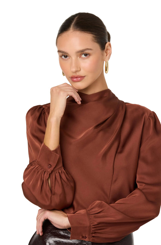 Woman wearing a brown blouse with puffed sleeves against a plain background