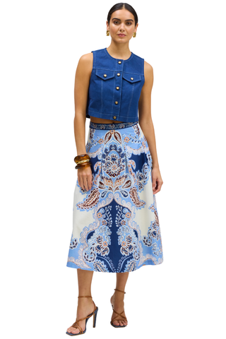 A model wearing a sleeveless blue denim vest and a high-waisted midi skirt with a blue, white, and beige paisley pattern, paired with brown strappy heels against a white background.