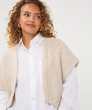 A chunky knit cardigan gilet in biscuit color hanging on a rack.
