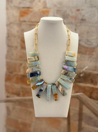 Necklace with multicolored stones on a mannequin bust against a brick wall background