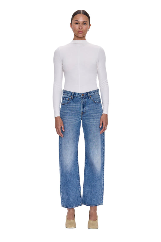 Person wearing a white long-sleeve top and blue jeans on a light gray background