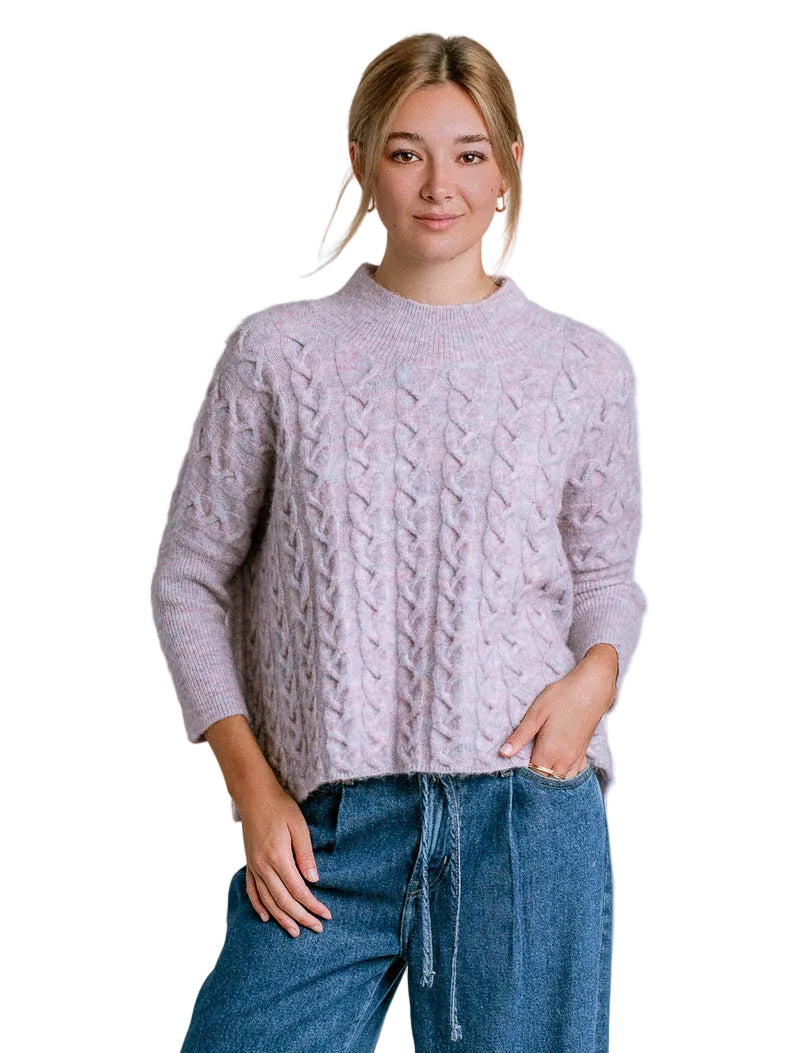 Woman wearing a cable knit sweater and jeans against a plain background