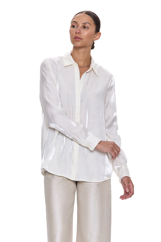 Woman wearing a white blouse and beige pants against a light gray background