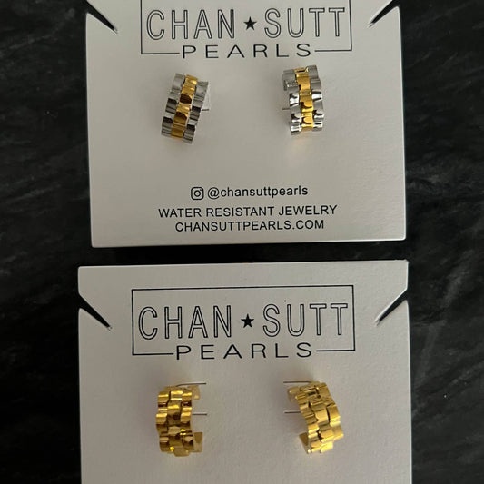 Gold and silver earrings on 'Chan Sutt Pearls' cards against a dark background