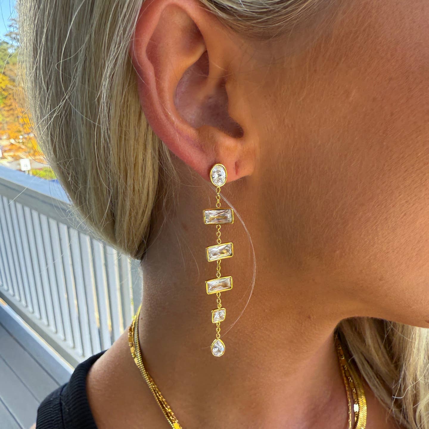 Close-up of a person wearing gold earrings with a blurred outdoor background