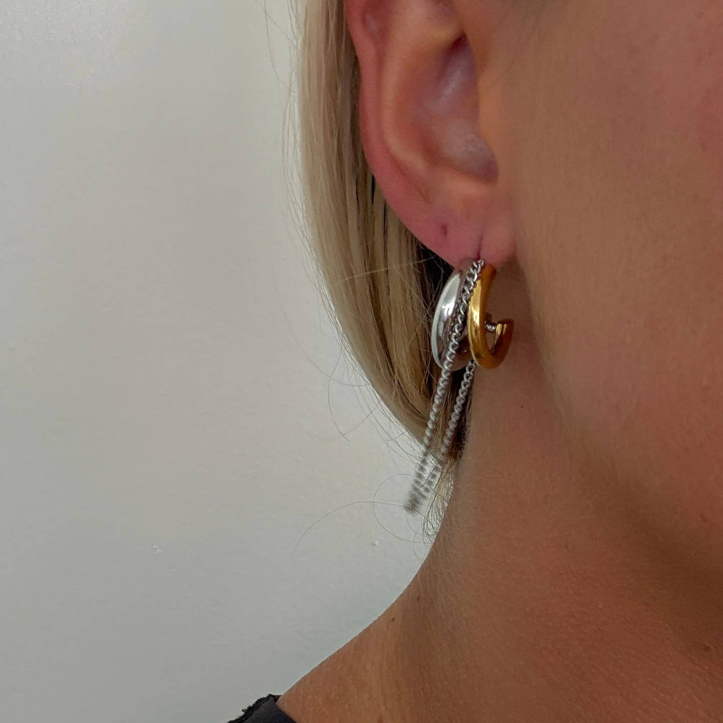 Close-up of an ear wearing a gold hoop earring with a clear chain.